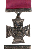 A bronze cross patt&eacute;e bearing the crown of Saint Edward surmounted by a lion with the inscription FOR VALOUR. A crimson ribbon is attached