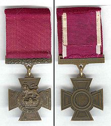 The obverse and reverse of the bronze cross patt&eacute;e medal; obverse showing the crown of Saint Edward surmounted by a lion with the inscription FOR VALOUR with a crimson ribbon; the reverse shows the inscription of the recipient on the bar connecting the ribbon with the regiment in the centre of the medal.