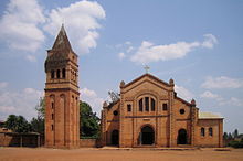 Photograph depicting the Catholic parish church in Rwamagana, Eastern Province, including the main entrance, fa&ccedil;ade, the separate bell tower, and dirt forecourt